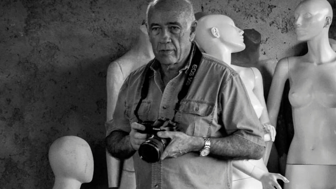 Alexis Pérez-Luna, con camisa clara y una cámara en las manos, posa entre maniquíes blancos en una foto en blanco y negro.