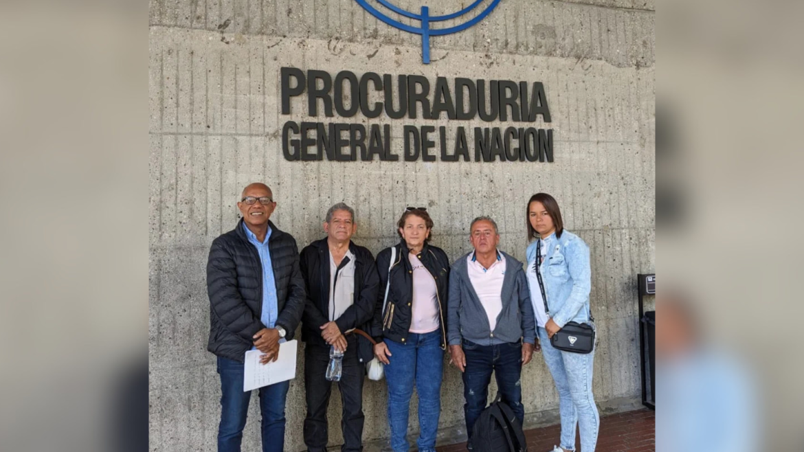 Cinco personas posan frente al cartel de la Procuraduría General de la Nación, en Colombia, bajo parte del escudo nacional.