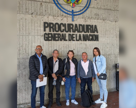 Cinco personas posan frente al cartel de la Procuraduría General de la Nación, en Colombia, bajo parte del escudo nacional.