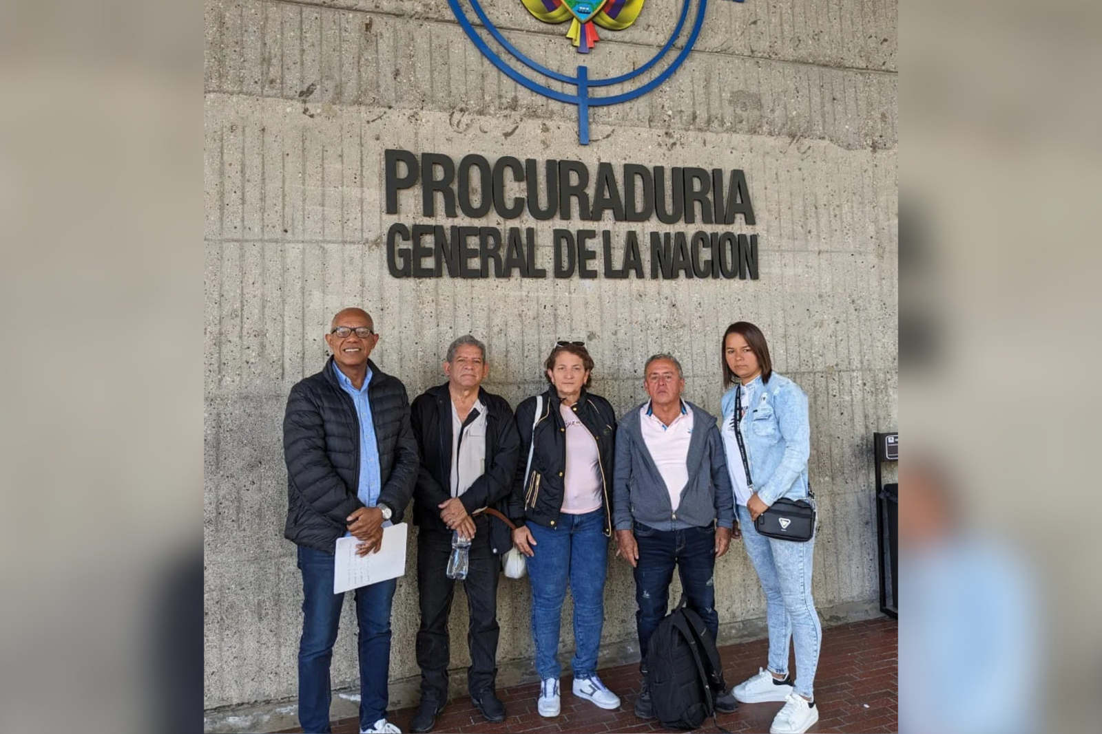 Cinco personas posan frente al cartel de la Procuraduría General de la Nación, en Colombia, bajo parte del escudo nacional.
