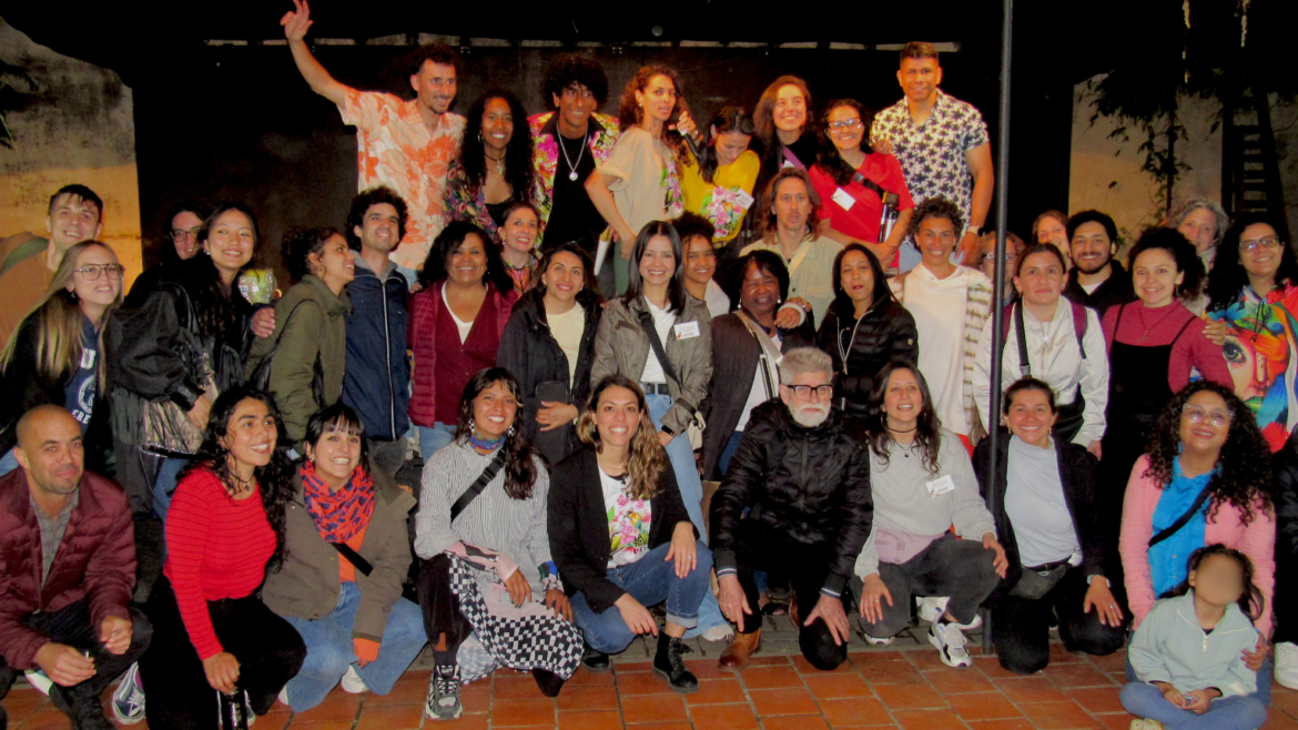 Foto grupal nocturna de artistas y participantes del Festival de Talento Migrante Latitudes en un patio con piso de baldosas