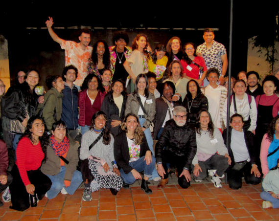 Foto grupal nocturna de artistas y participantes del Festival de Talento Migrante Latitudes en un patio con piso de baldosas