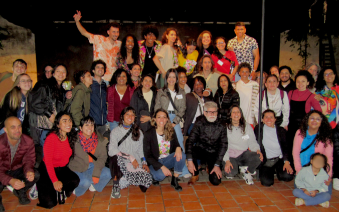 Foto grupal nocturna de artistas y participantes del Festival de Talento Migrante Latitudes en un patio con piso de baldosas