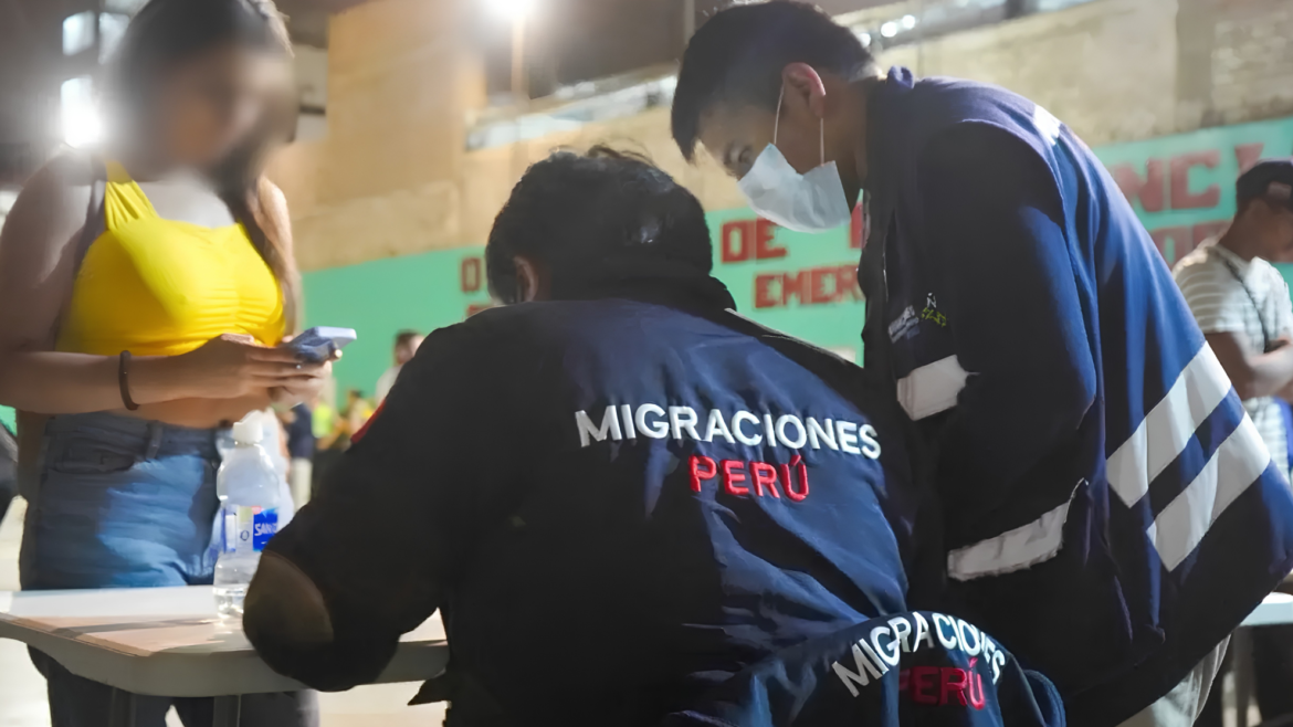 Agentes de Migraciones con chaquetas azules revisan documentos en una mesa nocturna junto a una mujer de remera amarilla con el rostro pixelado.