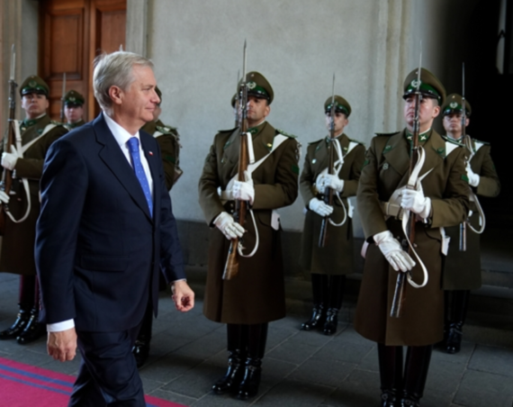 José Antonio Kast, de traje azul oscuro y corbata azul, camina por una alfombra roja frente a una guardia de honor de Carabineros en La Moneda.