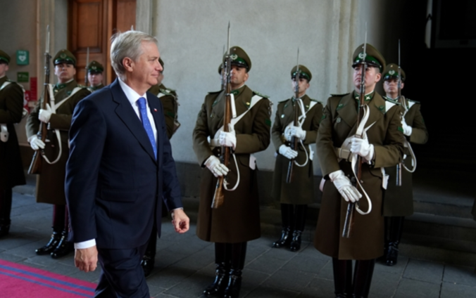 José Antonio Kast, de traje azul oscuro y corbata azul, camina por una alfombra roja frente a una guardia de honor de Carabineros en La Moneda.