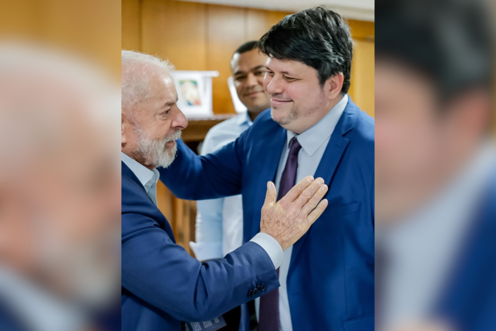 Luiz Inácio Lula da Silva apoya la mano en el pecho de Rogério Tomaz Júnior; ambos visten traje azul en una oficina con paneles de madera