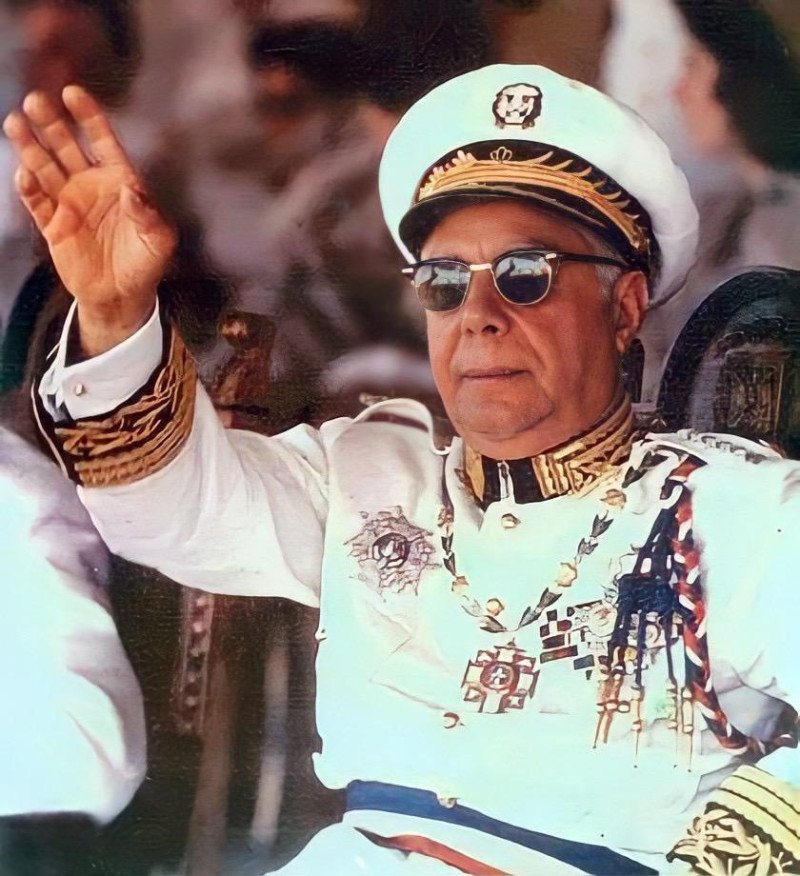 Rafael Leónidas Trujillo con uniforme blanco de gala, gorra, anteojos oscuros y condecoraciones, saludando con la mano en alto